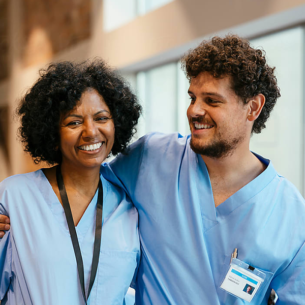 Friendly female and male nurses wearing blue uniform hugging while looking at camera at hospital